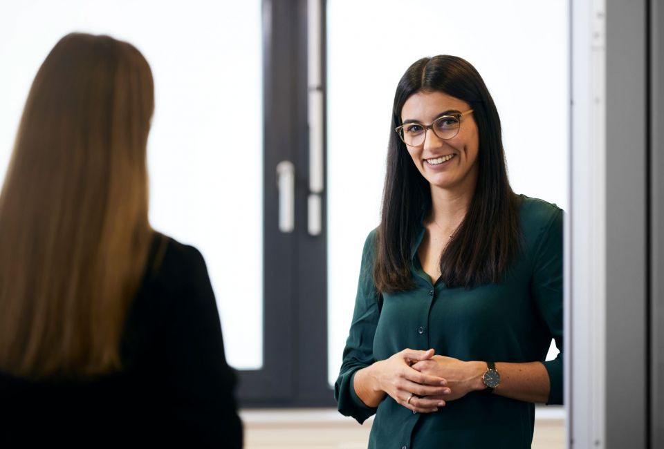 Frau mit Brille steht am Türrahmen und lächelt